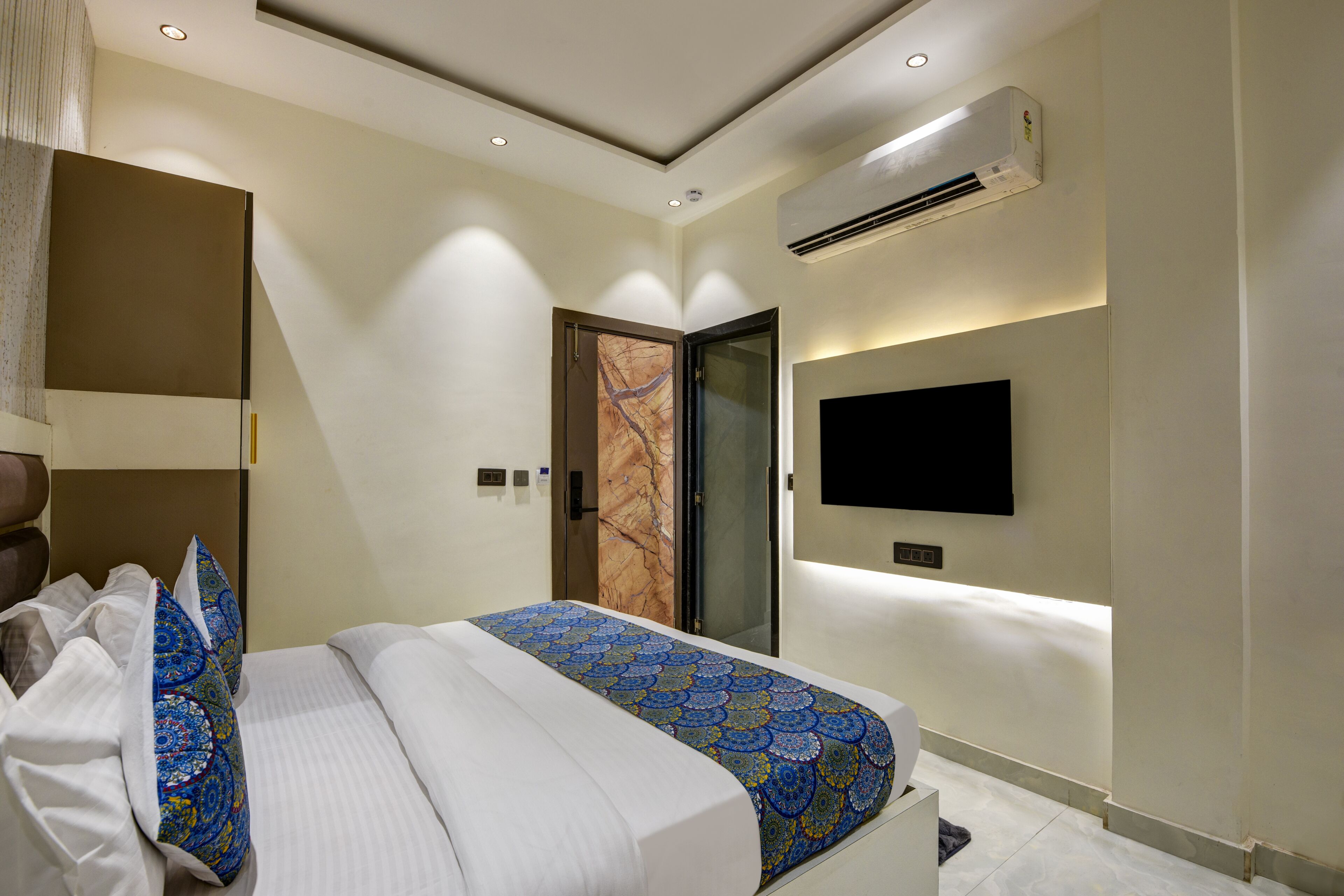 Une chambre d’hôtel moderne dotée d’un grand lit, d’un téléviseur à écran plat fixé au mur et d’un appareil de climatisation.