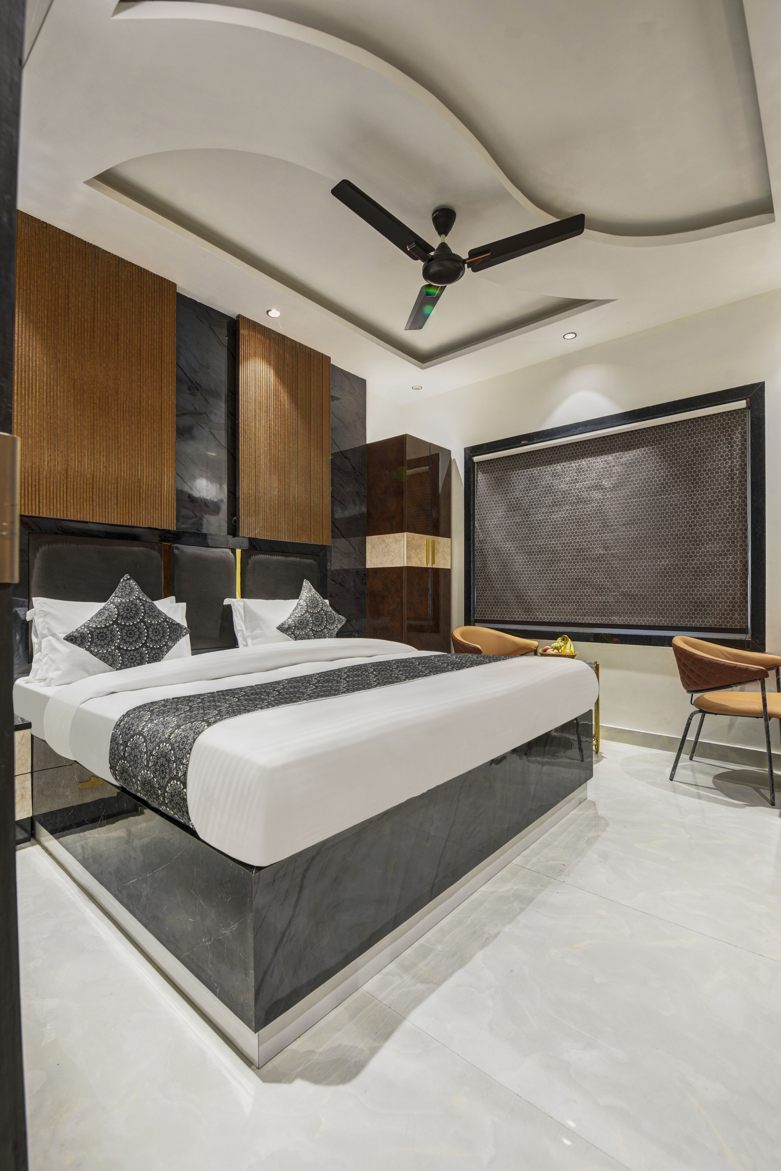A modern bedroom with a bed, a ceiling fan, a window with a view, and a seating area.