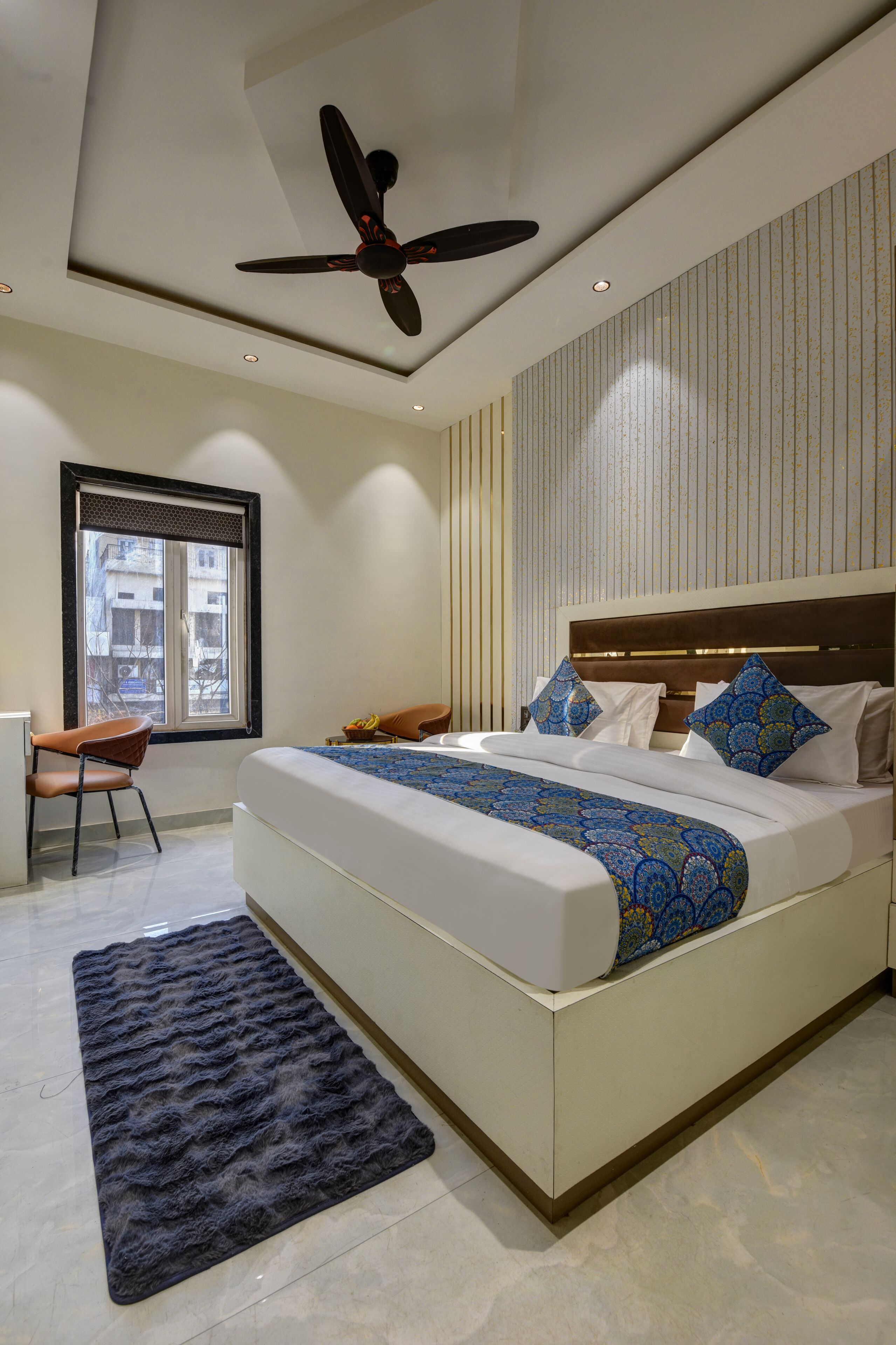 A modern bedroom with a large bed, a ceiling fan, a window, and a small desk.