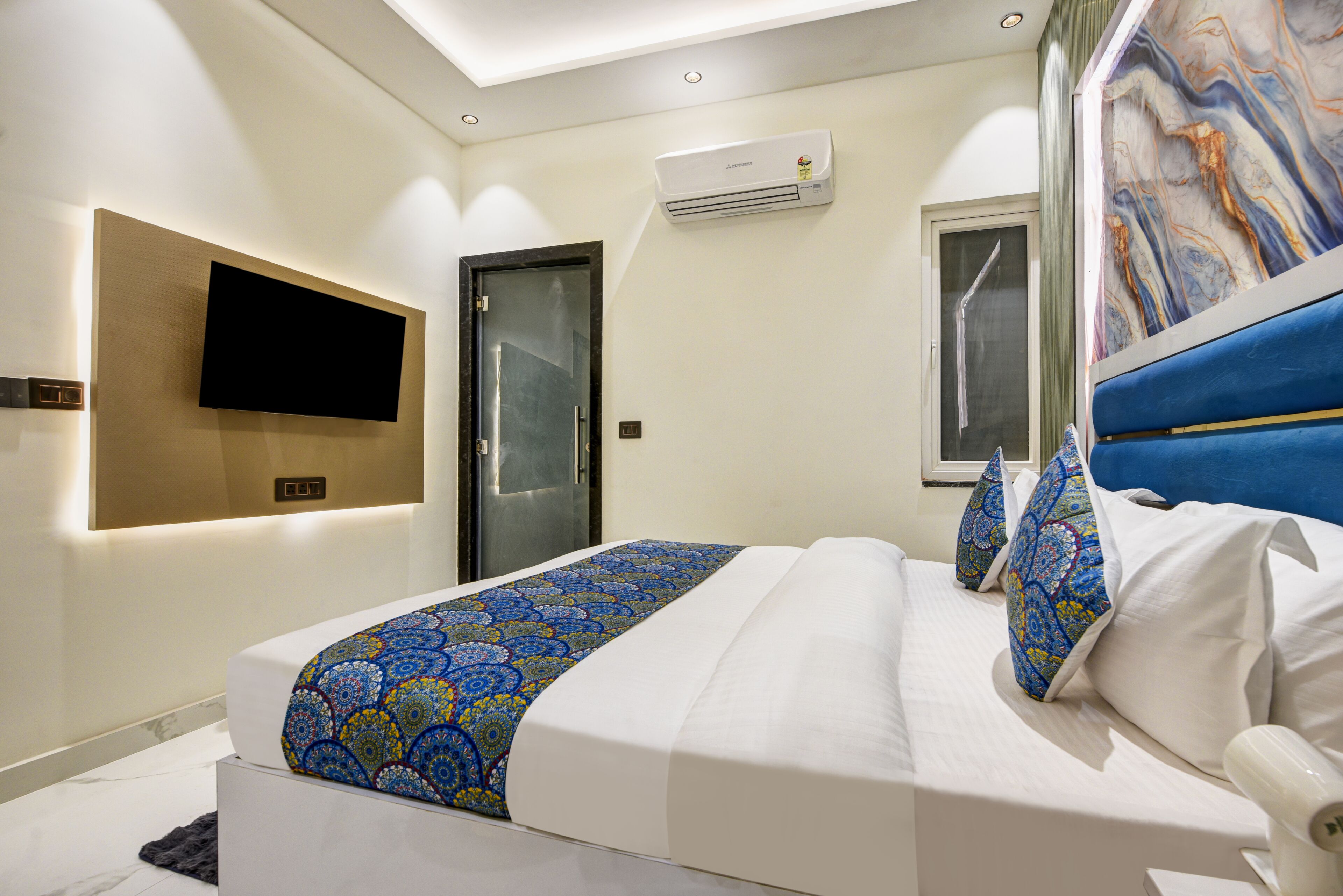 Una habitación de hotel moderna con una cama grande, un televisor de pantalla plana en la pared y una obra de arte con diseño de mármol.