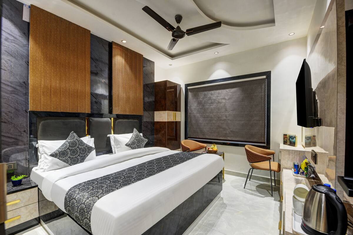 A modern hotel room with a large bed, a ceiling fan, a TV, a seating area, and a large window.