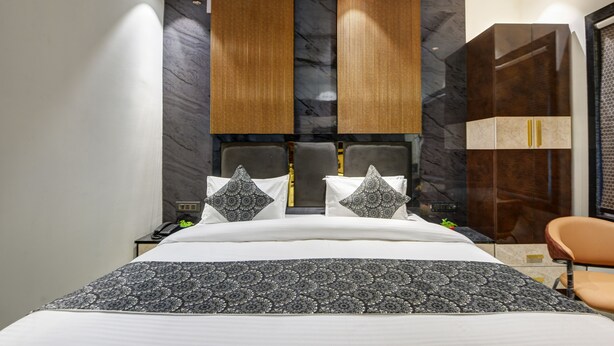 Habitación de hotel moderna con una cama grande, cabecero de paneles de madera verticales, pared de mármol y armario con tiradores dorados.