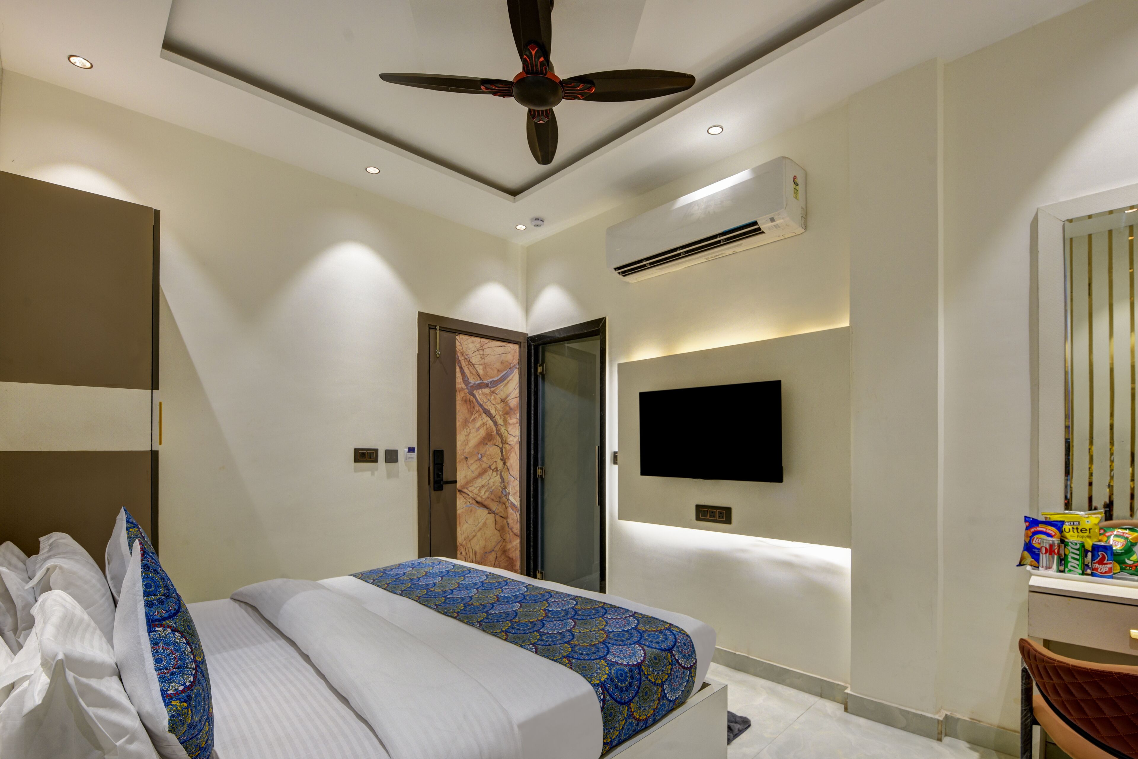 A modern hotel room with a bed, ceiling fan, air conditioning unit, and a flat-screen TV.