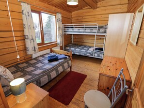 A cabin with a bunk bed, a single bed, a desk with a lamp, and a window with curtains. - Primrose Lodge (Evesham)