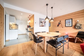 A modern kitchen with wooden walls, a dining area with a round table, and a red chair. - Apartment "Erin" with Mountain View, Private Terrace and Wi-Fi (Châtel)