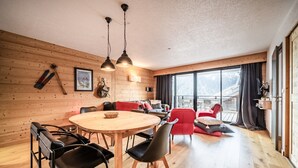 Una habitación acogedora con una pared de madera, una mesa redonda de madera con sillas, un sofá rojo y un ventanal con cortinas.