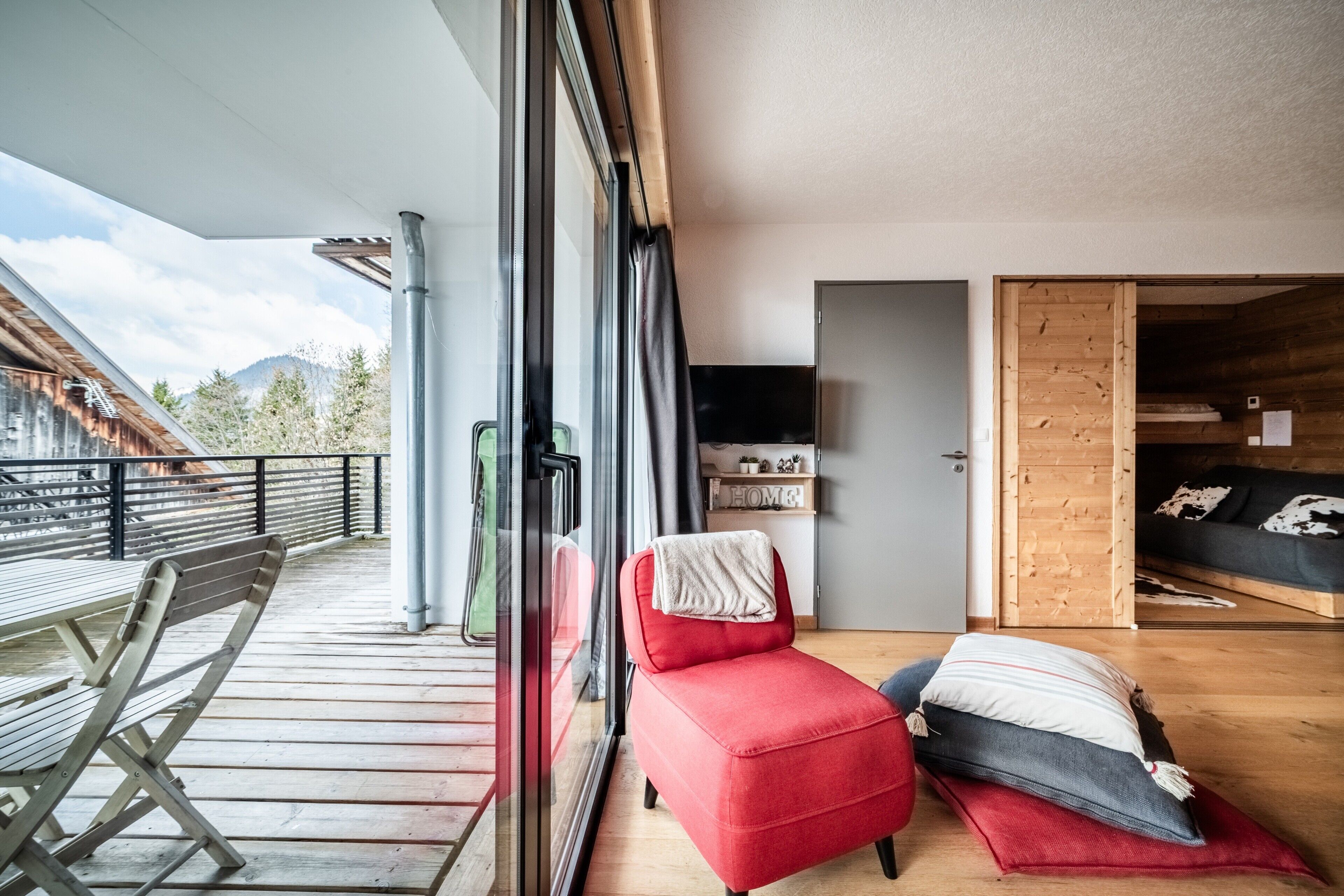 Quarto moderno com uma cadeira vermelha, um banco de madeira e vista para montanhas.