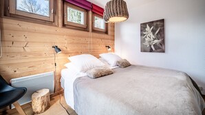 Un dormitorio con cama, dos ventanas, una lámpara de pared y un cuadro enmarcado.