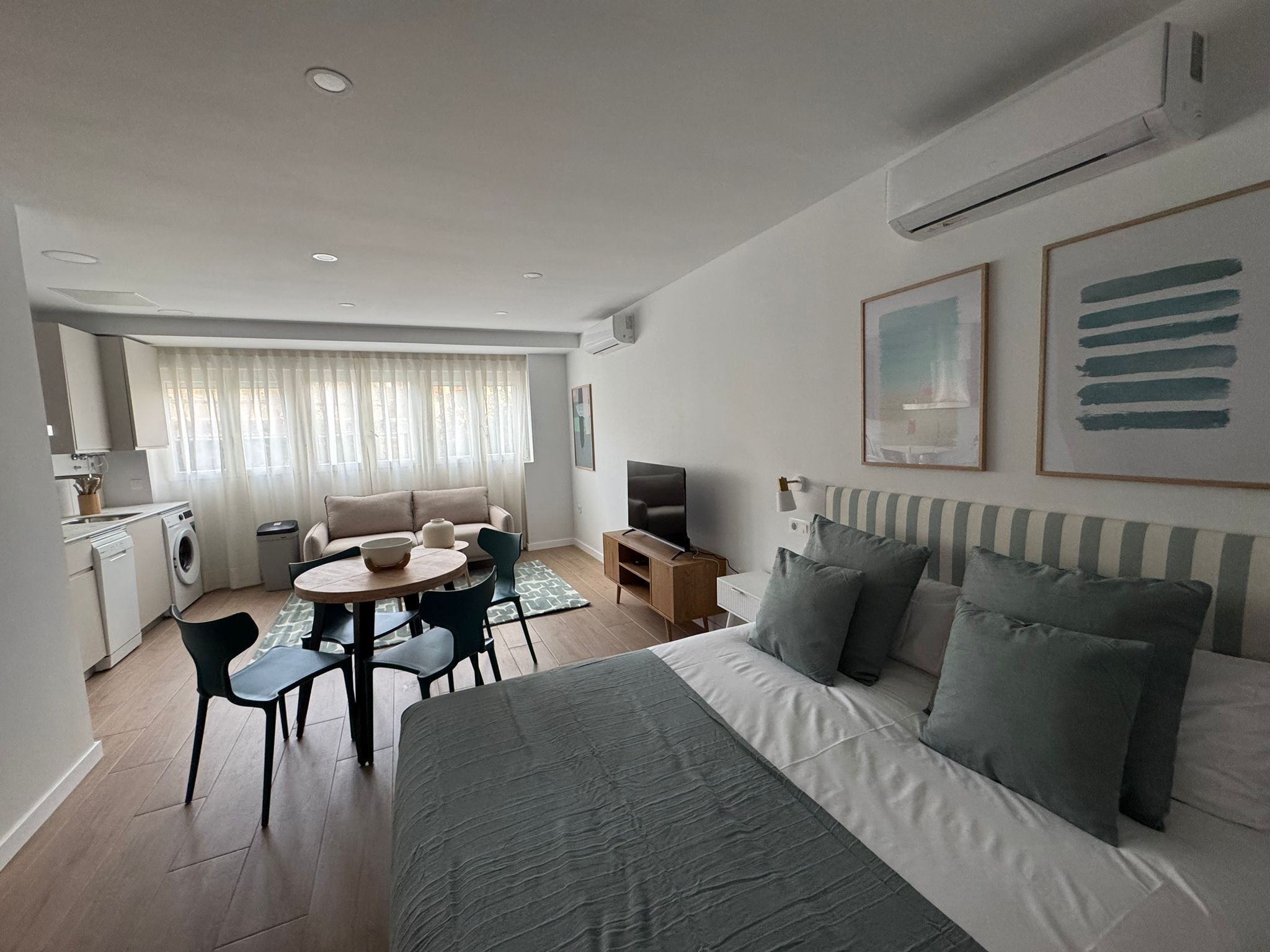 A modern, well-lit room with a bed, a TV, a dining area, and a kitchen.