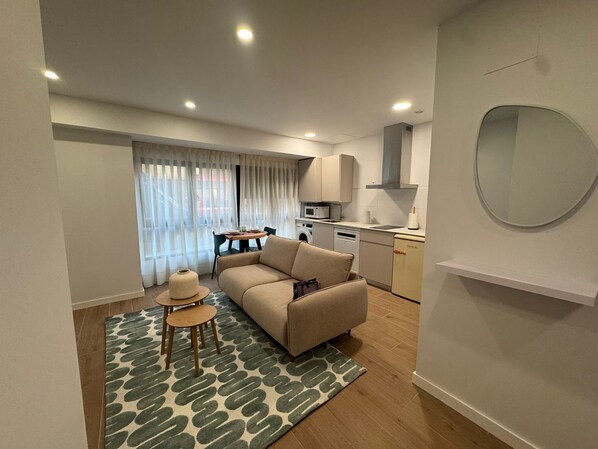 A compact living space with a sofa, a small dining table, a kitchen area with a microwave, and a washing machine. - Apartamentos Marcela by gaiarooms (León)