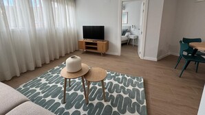 A modern living room with a TV, a sofa, a dining area with chairs, and a bedroom visible through an open door. - Apartamentos Marcela by gaiarooms (León)
