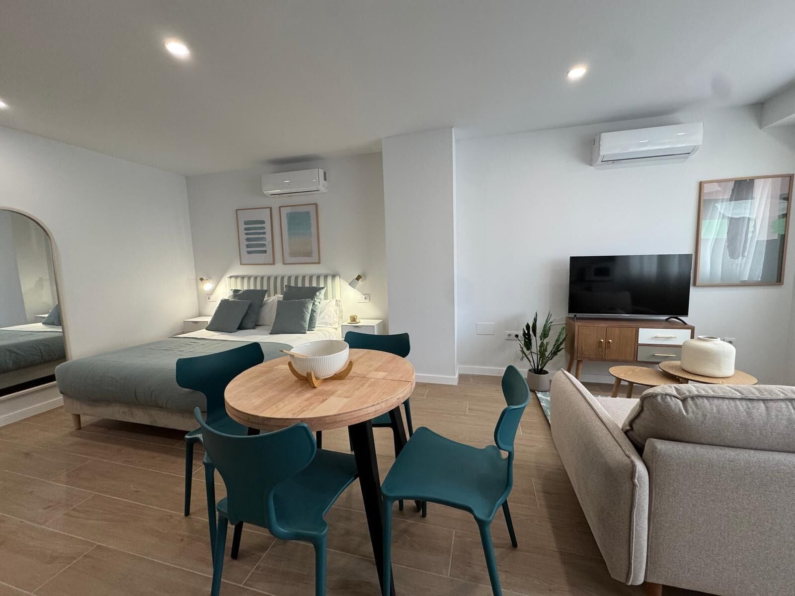 Una sala de estar moderna con un sofá, una mesa de comedor con sillas, un televisor y un equipo de aire acondicionado.