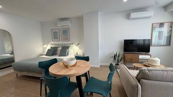 Una sala de estar moderna con un sofá, una mesa de comedor con sillas, un televisor y un equipo de aire acondicionado.