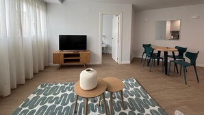 A modern living room with a flat-screen TV on a wooden stand, a dining area with a table and chairs, and a large mirror on the wall. - Apartamentos Marcela by gaiarooms (León)
