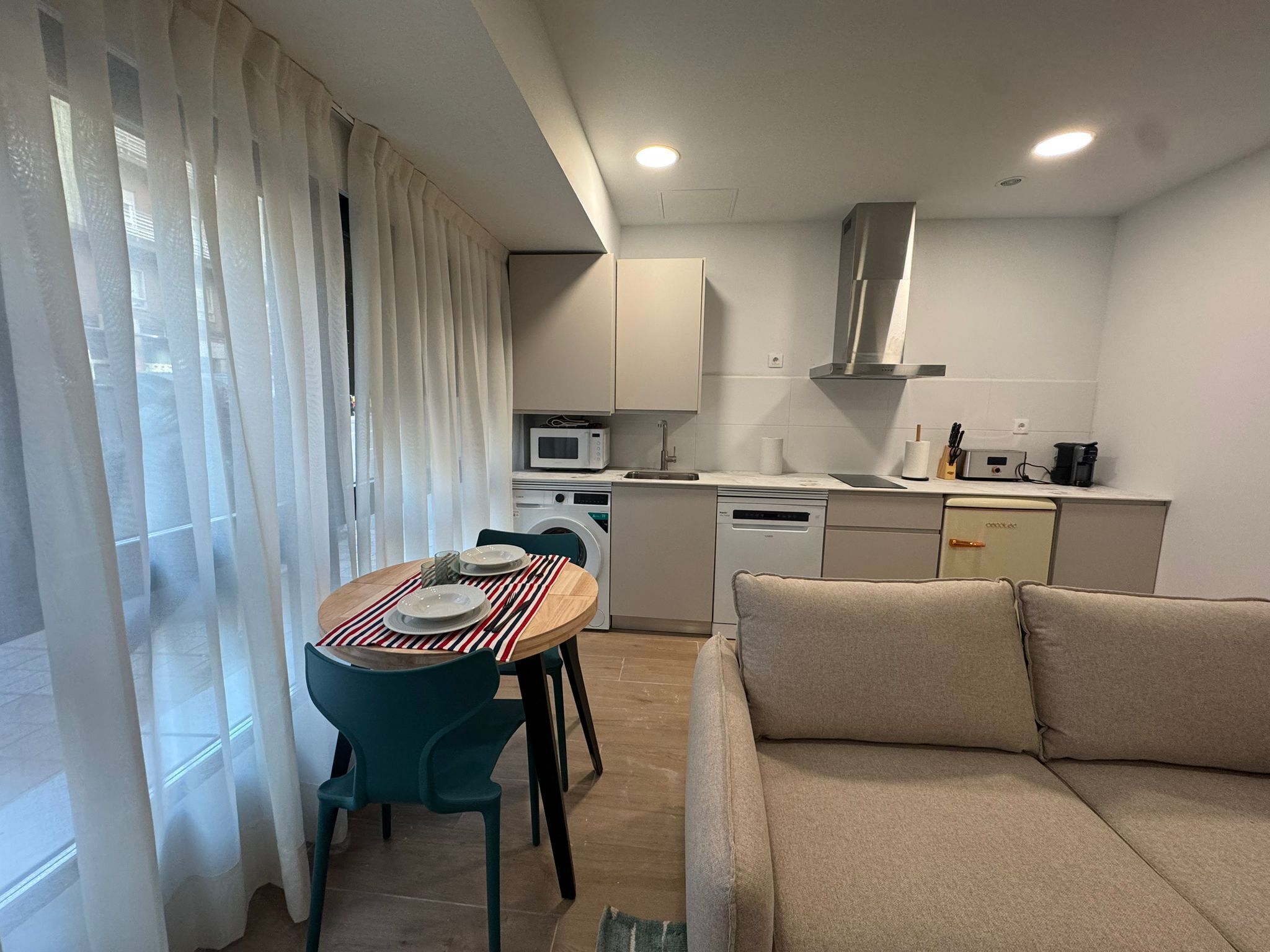 A compact kitchen with a dining area, a sofa, and a washing machine.