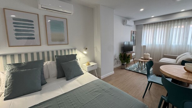 A modern hotel room with a bed, bedside table, TV, and a dining area with a table and chairs. - Apartamentos Marcela by gaiarooms (León)