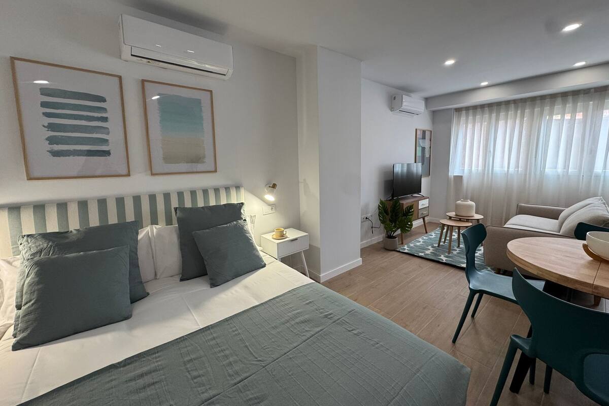Een moderne hotelkamer met een bed, nachtkastje, televisie en een zithoek met een tafel en stoelen.