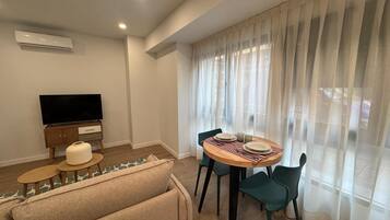 Una sala de estar moderna con una televisión de pantalla plana, un sofá, una mesa de comedor con sillas y cortinas de gasa.