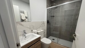 A modern bathroom with a marble vanity, a toilet, and a glass-enclosed shower. - Apartamentos Marcela by gaiarooms (León)