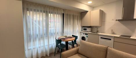 Un espacio habitable compacto con sofá, mesa de comedor, lavadora y microondas en la kitchenette.