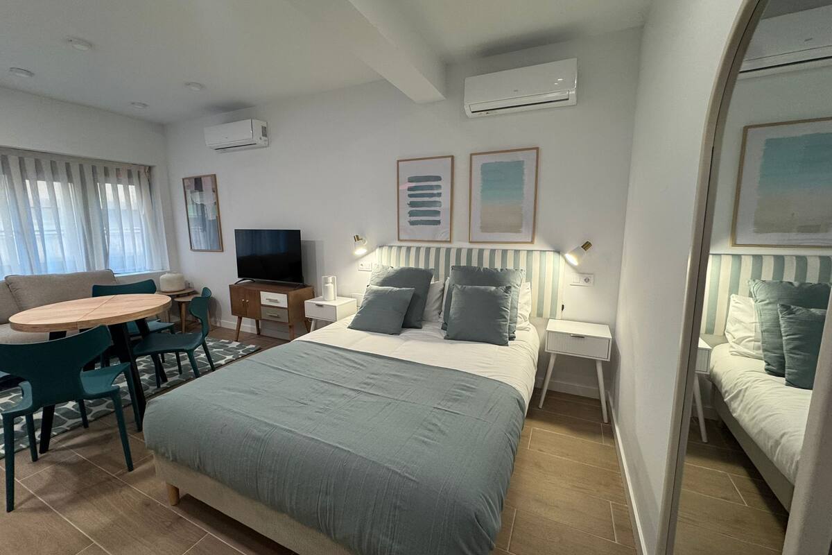 Een hotelkamer met een bed, een televisie, een eettafel met stoelen en een bijzettafeltje met een lamp.