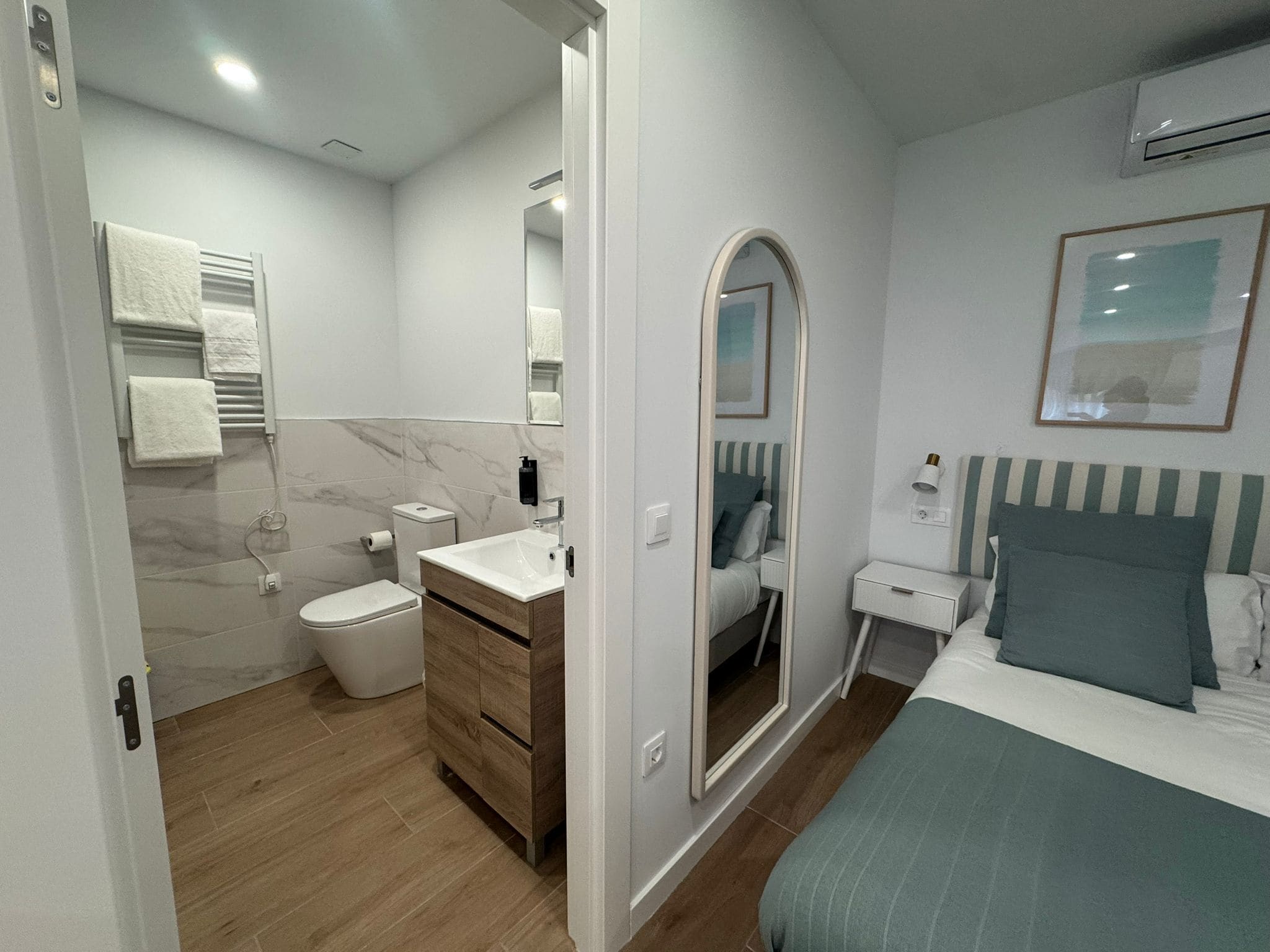 Una habitación de hotel moderna con baño, una cama, una mesita de noche y un espejo.