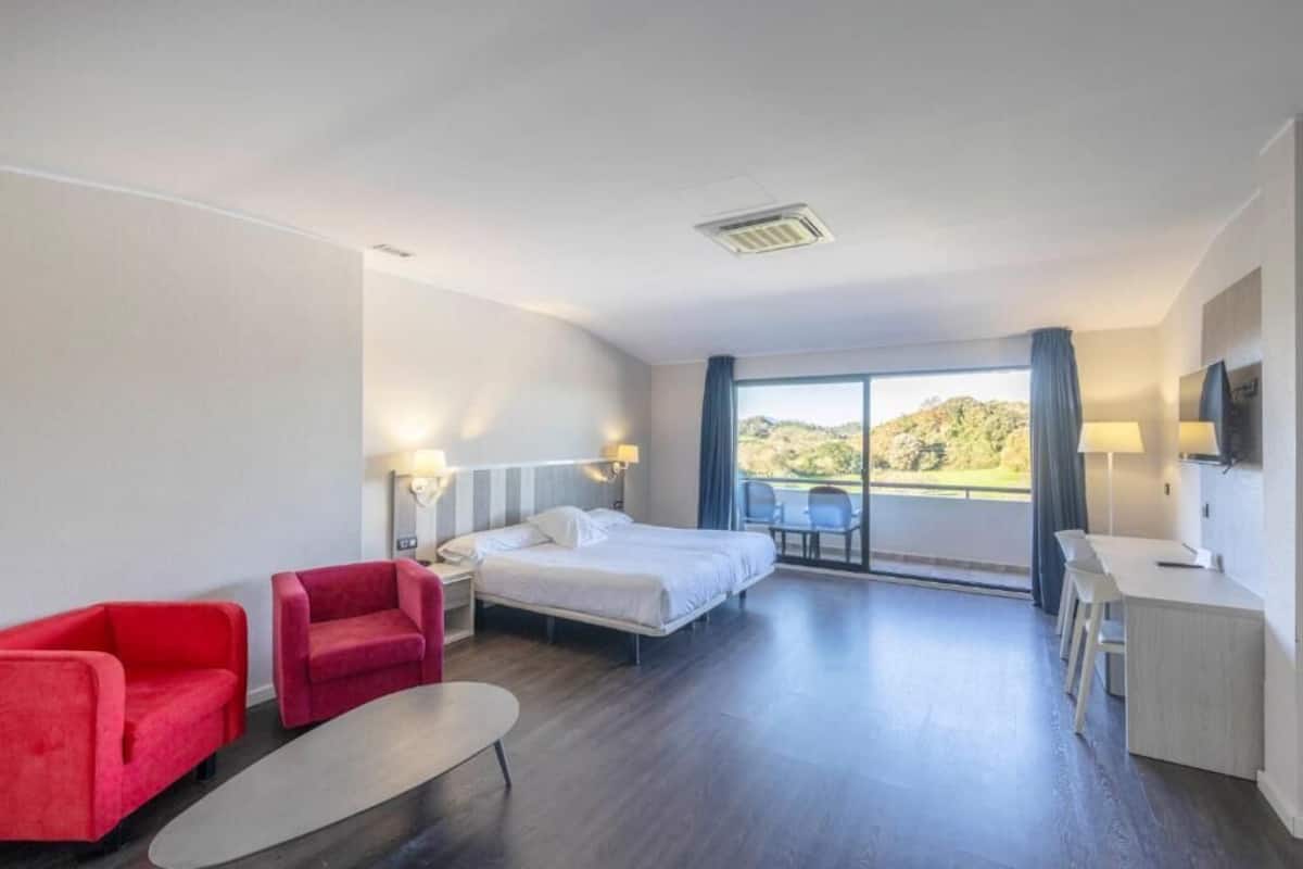 A hotel room with a bed, a desk, a chair, a small table, and a window with a view.