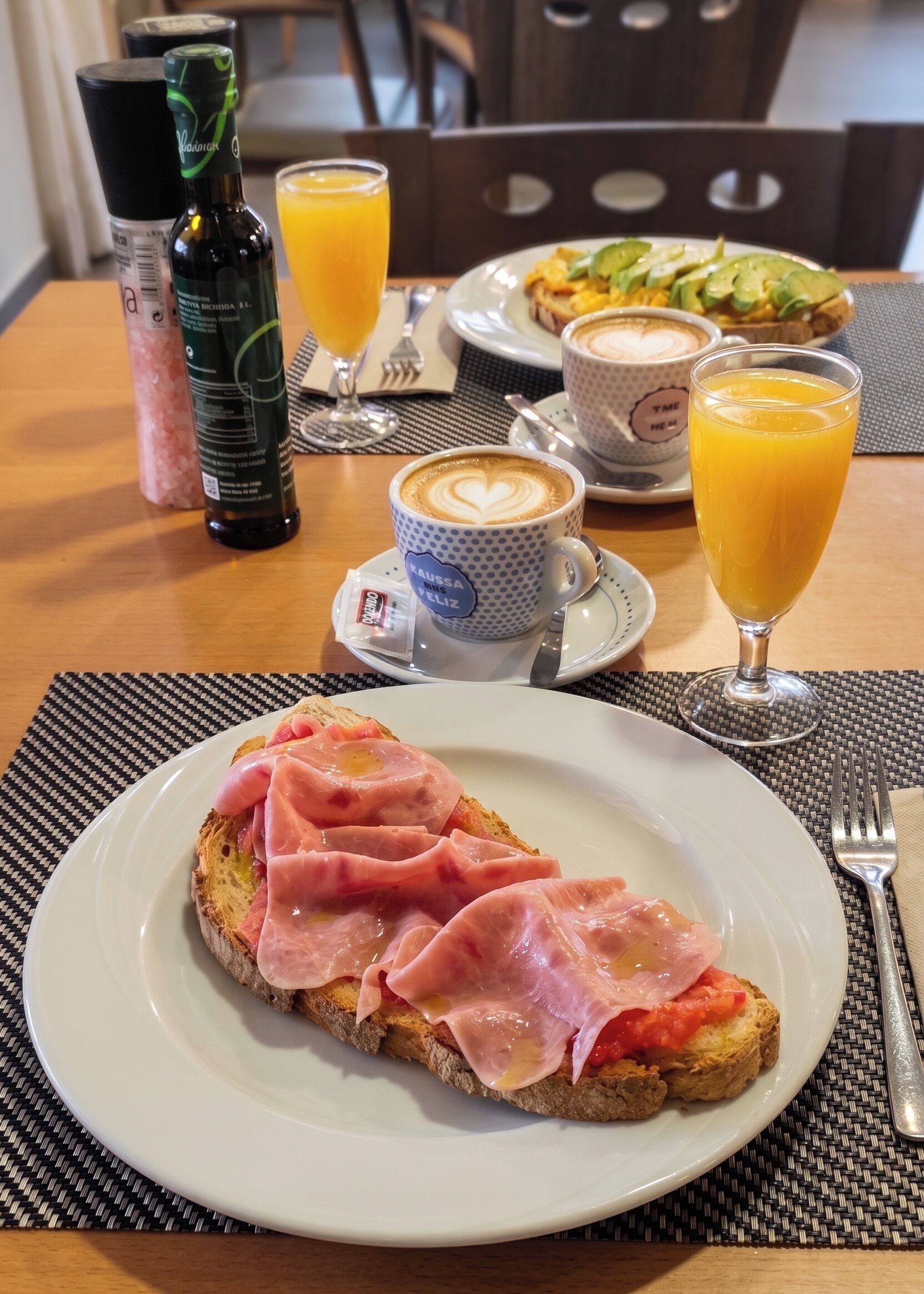 Una mesa de desayuno con tostadas, jamón y un vaso de zumo de naranja.