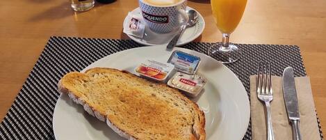 Un desayuno con tostadas, café, jugo de naranja y aderezos en un plato.