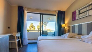 A hotel room with two beds, a desk, a chair, and a balcony with a view of palm trees. - Hotel La Palma de Llanes by gaiarooms (Llanes)