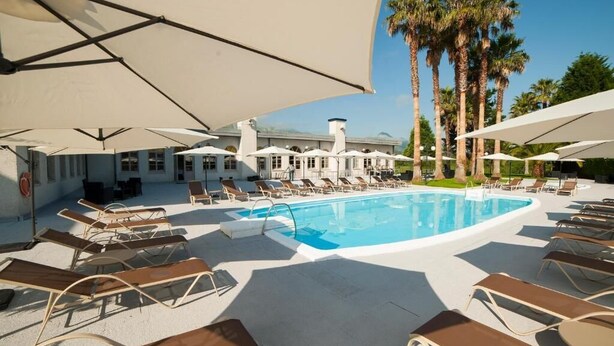 A pool area with sun loungers and umbrellas, surrounded by palm trees and a building in the background. - Hotel La Palma de Llanes by gaiarooms (Llanes)