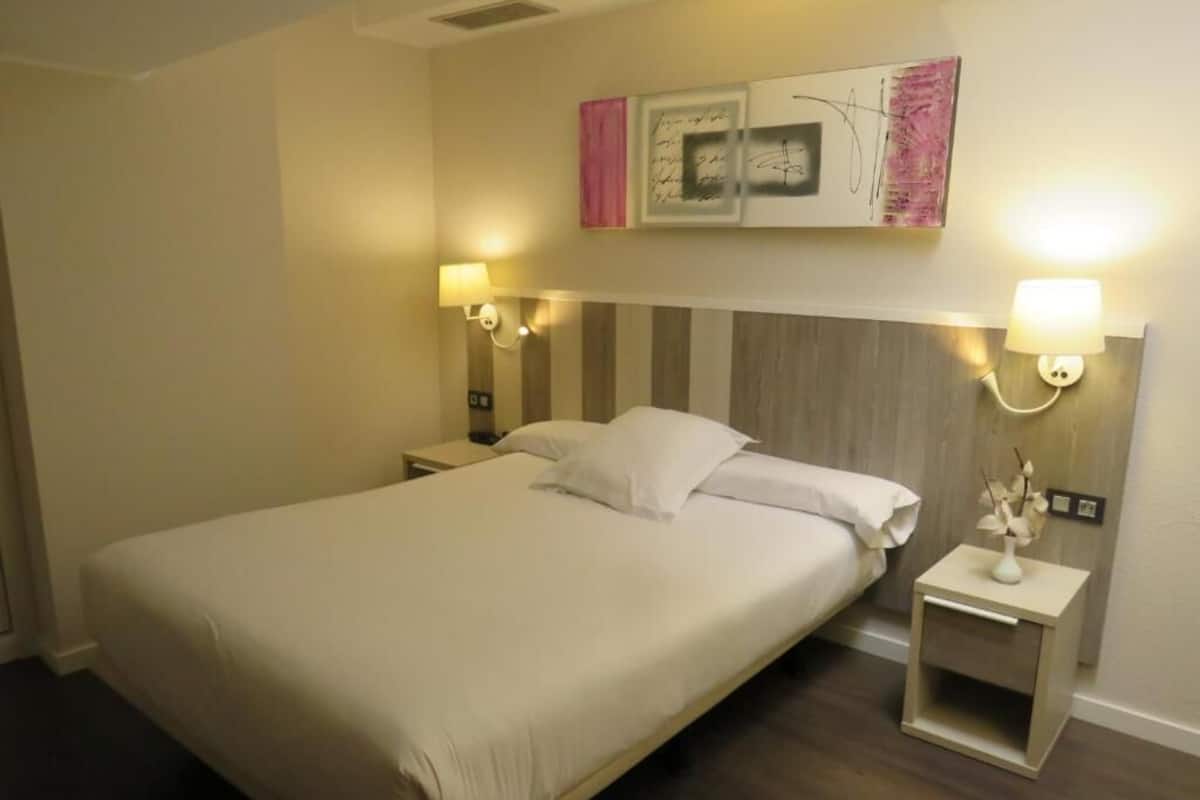 A hotel room with a large bed, two bedside tables, and wall-mounted lamps.