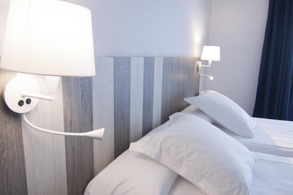 A hotel room with a bed, white bedding, a wall-mounted lamp, and a striped headboard.