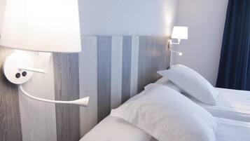 A hotel room with a bed, white bedding, a wall-mounted lamp, and a striped headboard.