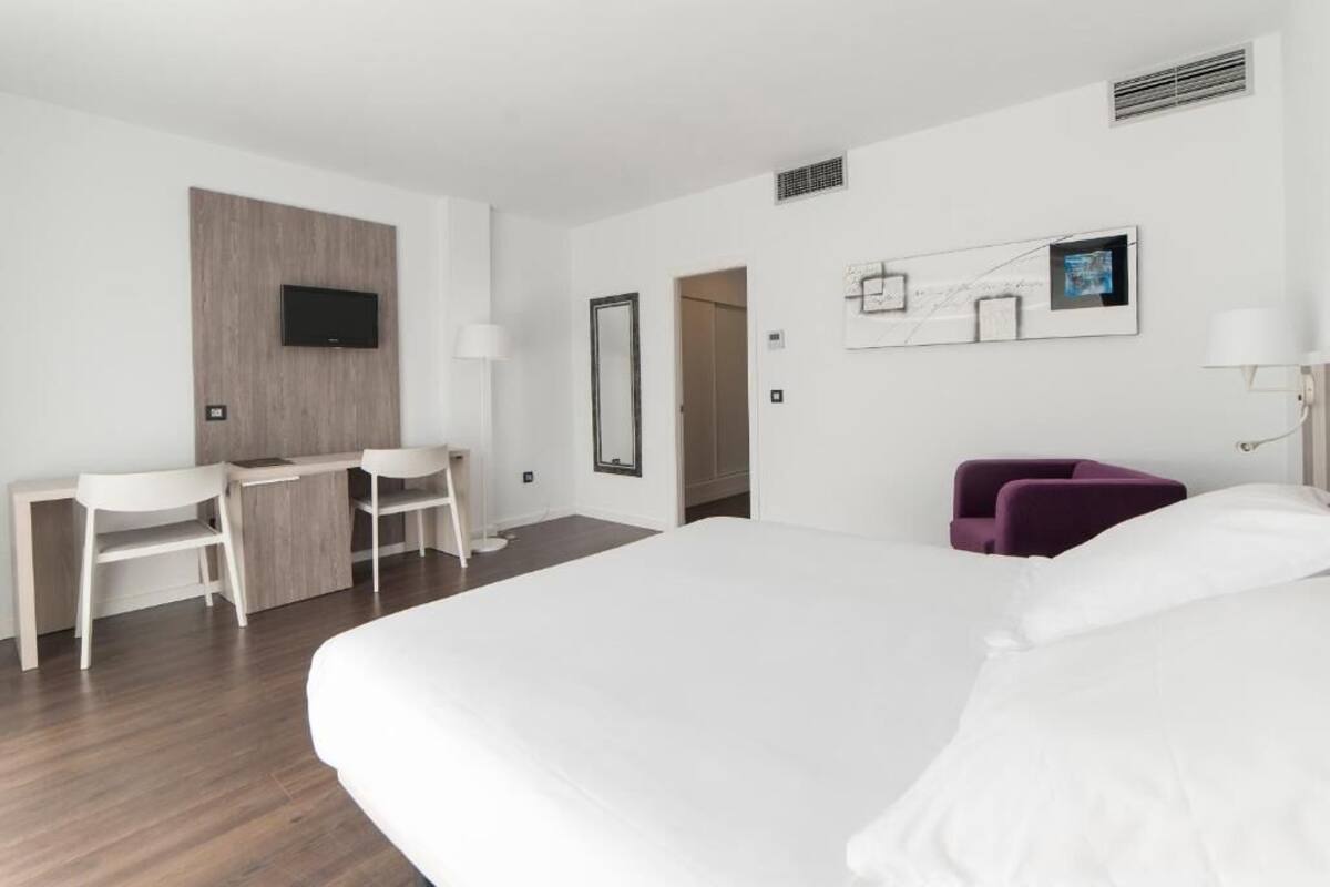 A hotel room with a bed, a desk with chairs, a TV, and a door leading to another room.