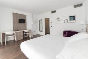 Habitación de hotel con cama, escritorio, sillas, televisor y puerta que da a otra habitación.
