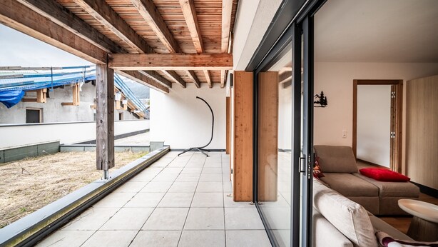A modern interior with a wooden ceiling, a sliding glass door leading to a balcony, and a beige sofa with red cushions.