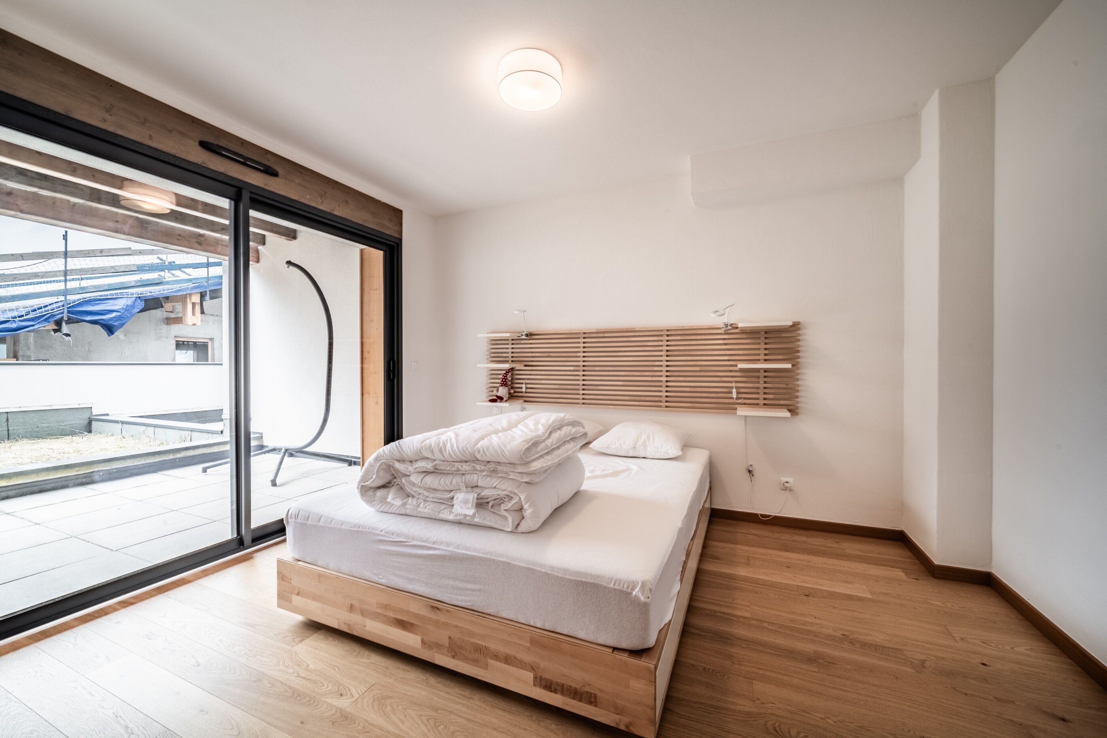 Une chambre moderne avec un lit en bois, une grande fenêtre et une vue sur l’extérieur.