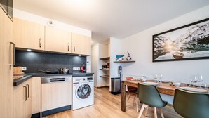 A modern kitchen with a washing machine, wooden cabinets, and a dining area with a table set for four.