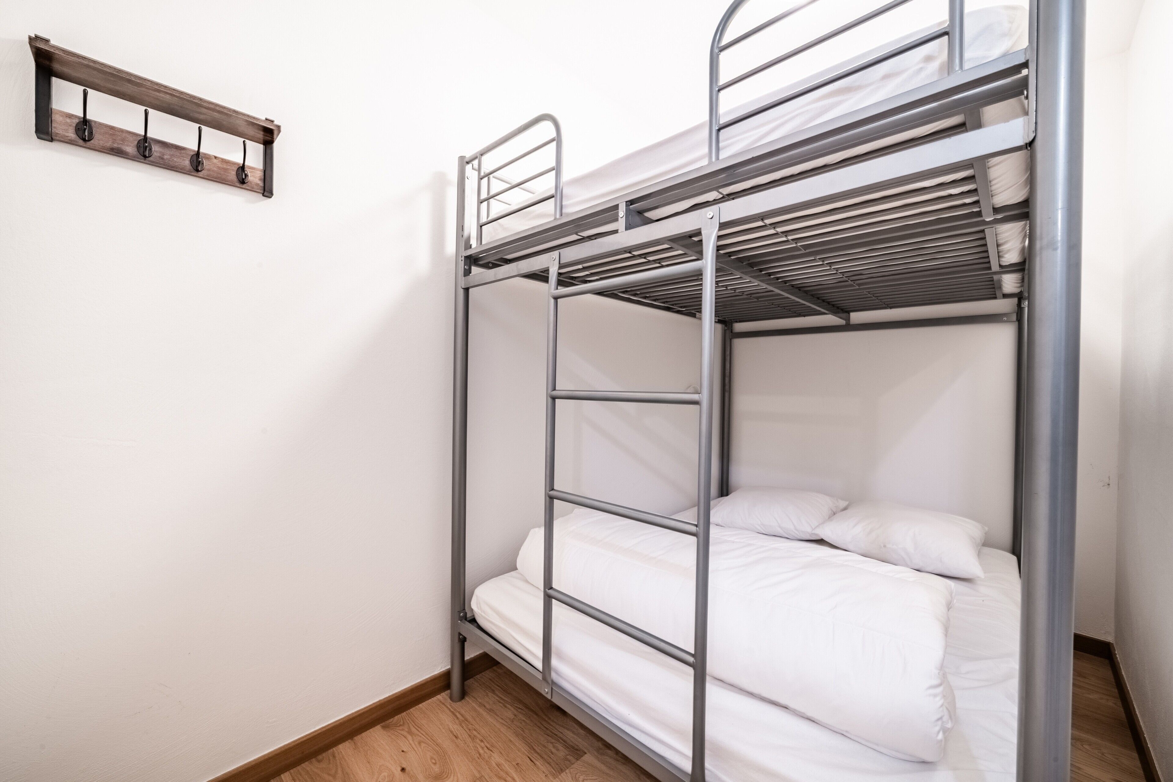 A bunk bed with a metal frame, white bedding, and a wooden shelf above.