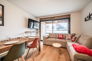 Un salon moderne avec une table à manger en bois, un canapé et un téléviseur fixé au mur.