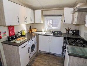 A compact kitchen with a washing machine, a stove, a sink, and a window. - Laurel Lodge (Evesham)