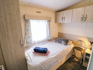 A bedroom with a bed, a window with curtains, a bedside table with a lamp, and a wardrobe. - Laurel Lodge (Evesham)