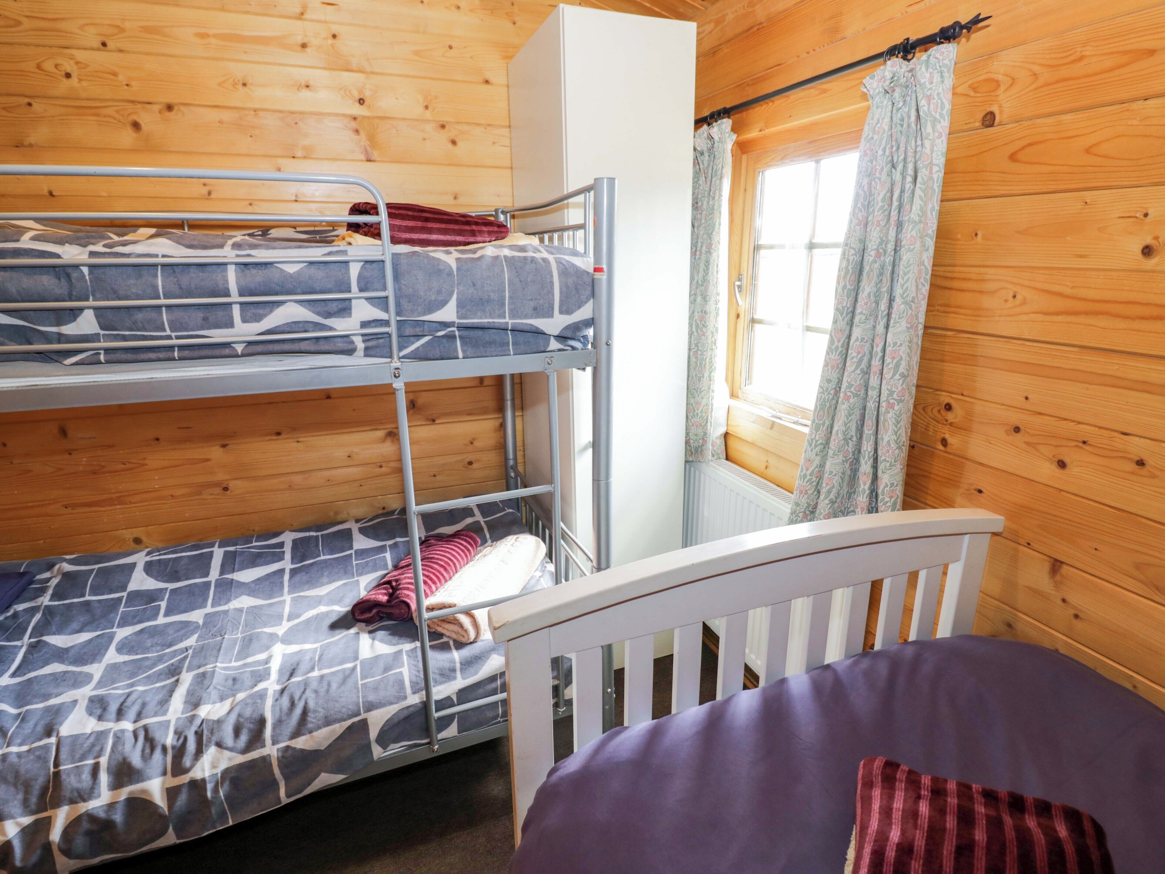 Une chambre avec un lit superposé, une fenêtre, des murs en bois et une armoire blanche.