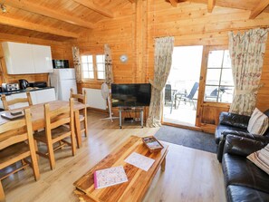 A wooden cabin interior with a dining area, a living room with a sofa, a TV, and a kitchen area. - Oak Lodge (Evesham)
