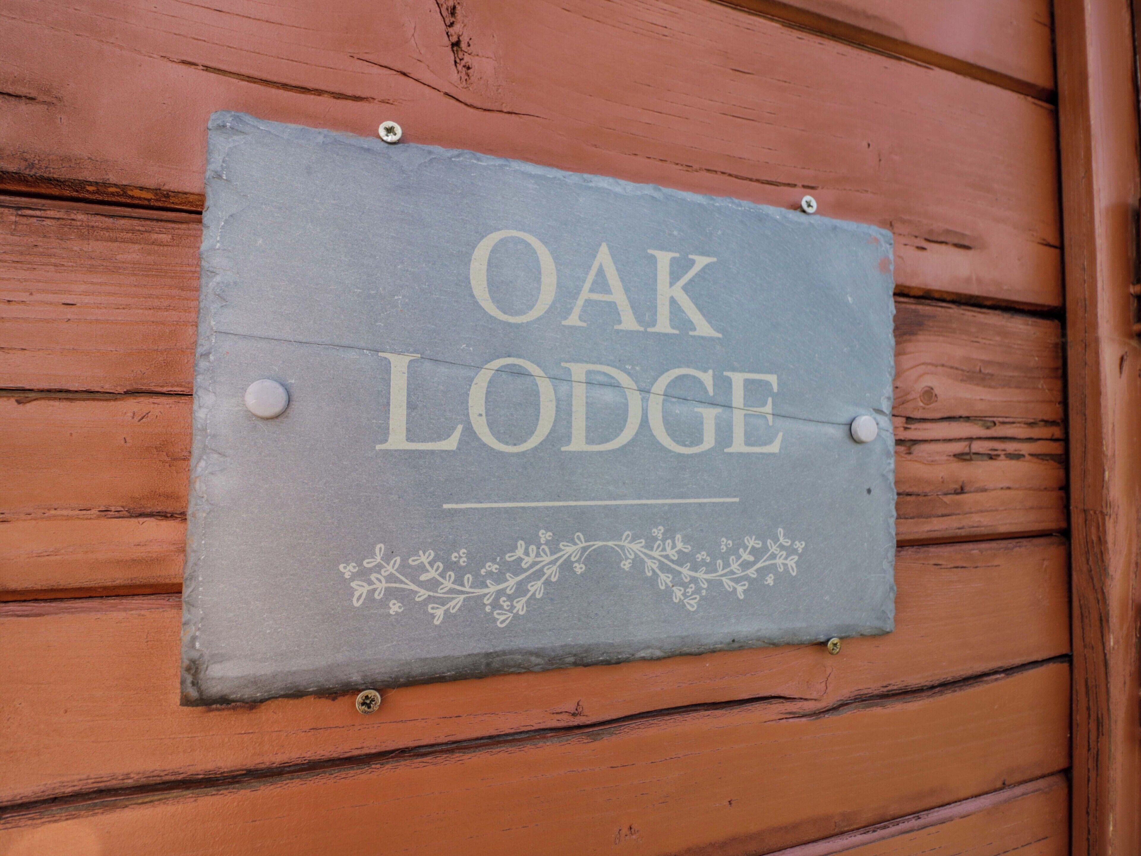 A slate sign with 'OAK LODGE' written on it, mounted on a wooden wall with visible horizontal planks.