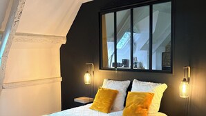 A bedroom with a bed, pillows, a bedside table, a nightstand, a window, and a wooden floor.
