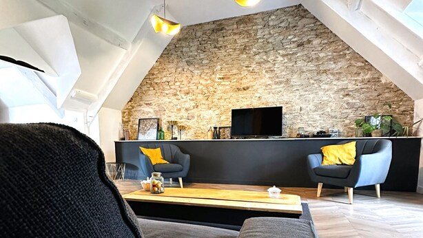 A loft-style living room with a stone wall, a flat-screen TV, and modern furniture.