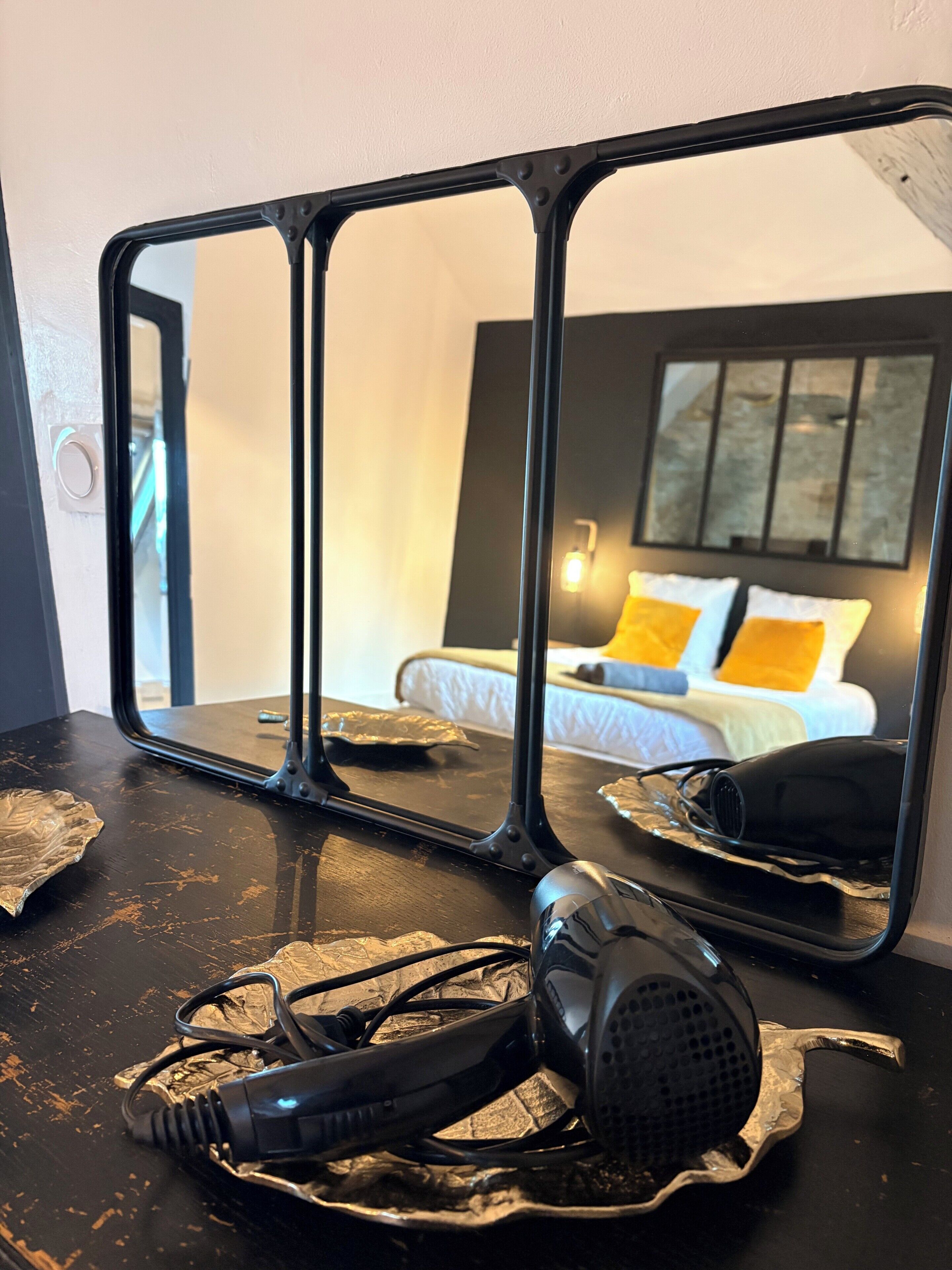 Quarto com cama, espelho e mesa com secador de cabelo e fones de ouvido.