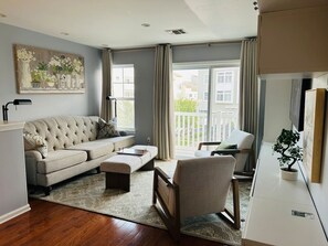 A living room with a sofa, ottoman, armchair, and a potted plant.